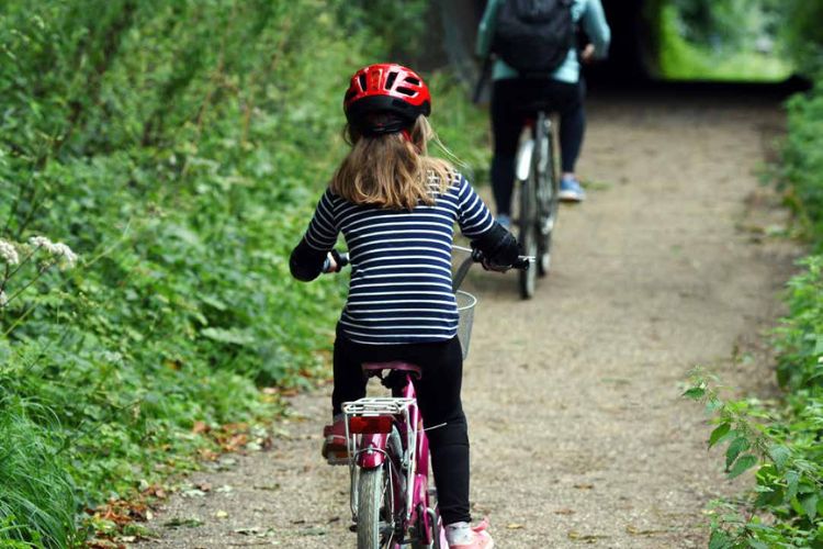 Photo of the back of a little girl and an older woman cycling down a cycle path, foilage either side